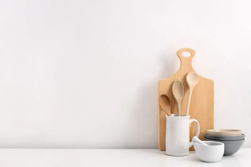A kitchen countertop with a cutting board, pitcher, bowls, wooden spoons, and a mortar and pestle.