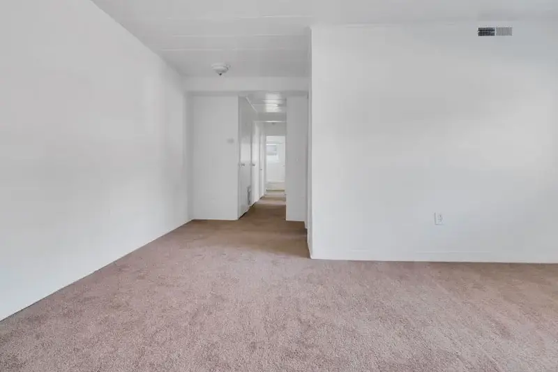 A living room with new carpet flooring leading to a hallways with access to several bedrooms.