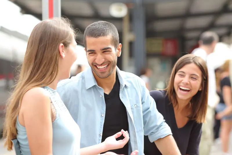 Three people smiling and talking in a public space.