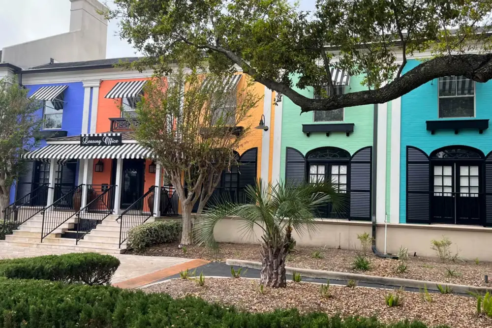 A row of colorful retail shops in a shopping plaza with trees and plants.