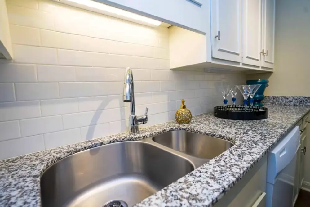 A kitchen with a double-basin sink, quartz countertops, white cabinets, and a dishwasher.