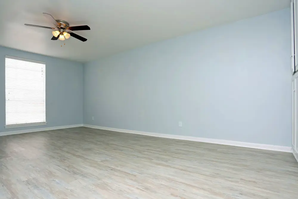A large room with a window, hardwood-style flooring, a ceiling fan, and cabinets for storage space.