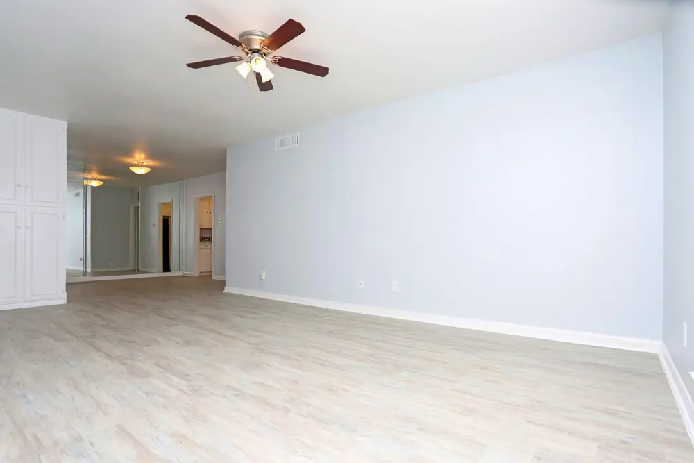 A large living room with a ceiling fan, storage cabinets, and hardwood-style flooring with access to a hallway