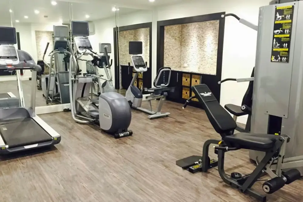 A fitness center with hardwood-style flooring, recessed lighting, weight and cardio machines, a large mirror, and storage compartments.