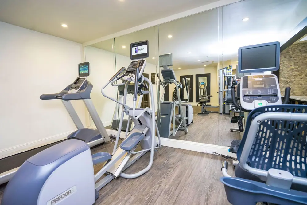 A fitness center with hardwood-style flooring, recessed lights, large mirrors and three cardio machines.